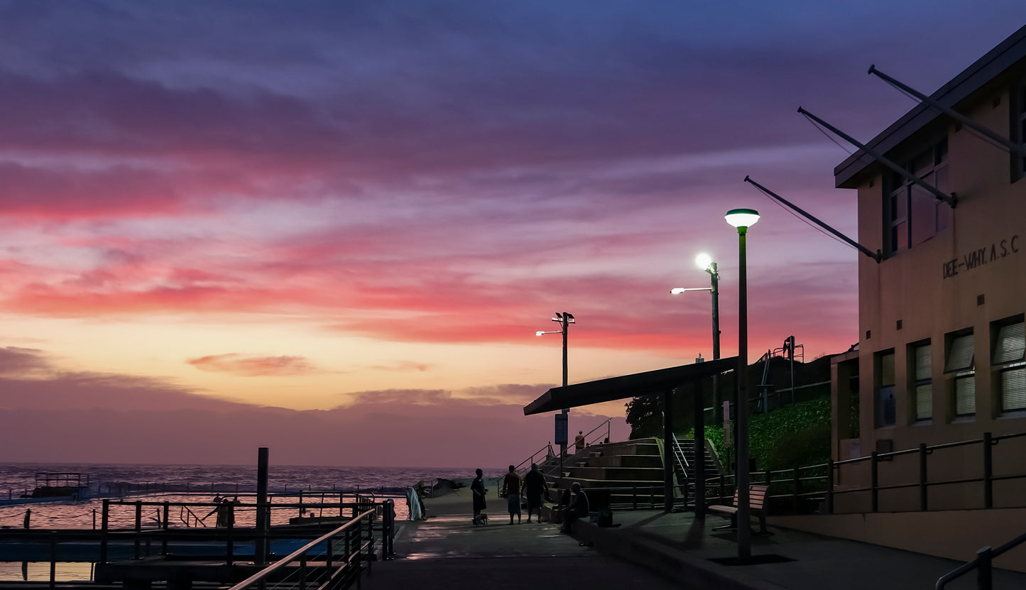 Surfers and swimmers in golden-hour beach light.